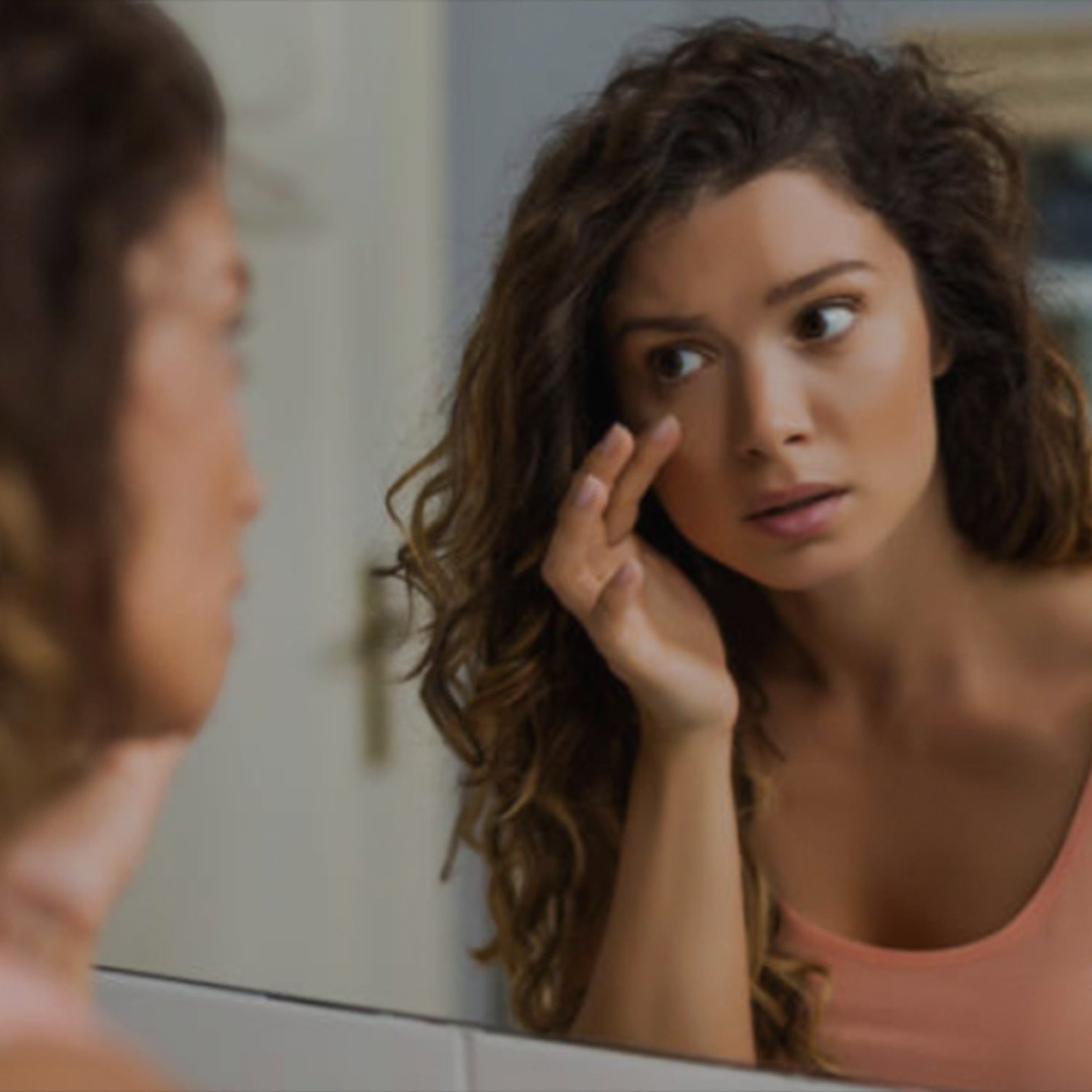 Das Bild zeigt eine junge Frau in einem Moment der Selbstreflexion, während sie konzentriert ihre Augen im Spiegelsbild untersucht. Es könnte Augengesundheit oder Suche nach persönlicher Erkenntnis symbolisieren.